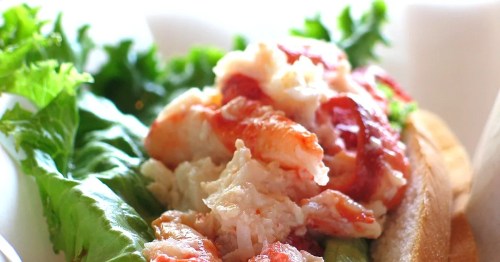 A close-up of a lobster roll topped with fresh lobster meat and served on a bed of lettuce.