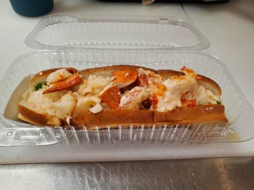 A lobster roll in a clear container, filled with chunks of lobster meat on a toasted bun.