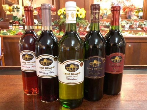 Five bottles of Long Hollow wine in various colors, including red, white, and rosé, displayed on a wooden counter.