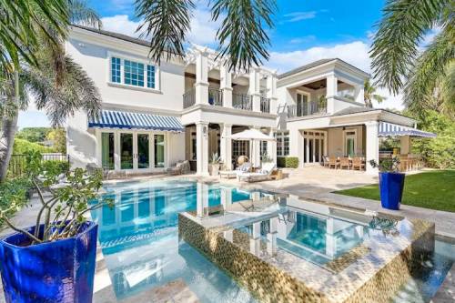 Luxurious home with a pool, palm trees, and outdoor seating in a sunny, landscaped backyard.