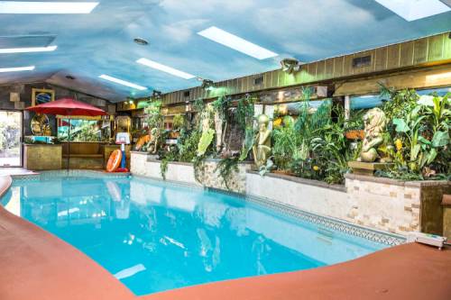 Indoor swimming pool surrounded by lush plants, sculptures, and colorful decor under a bright blue ceiling.