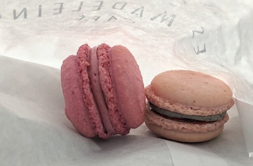 Two macarons, one pink and one beige with a green filling, resting on white parchment paper.