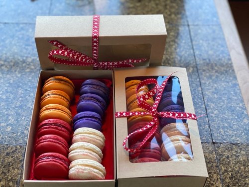 Two boxes of colorful macarons tied with red ribbon, featuring orange, purple, and assorted flavors.