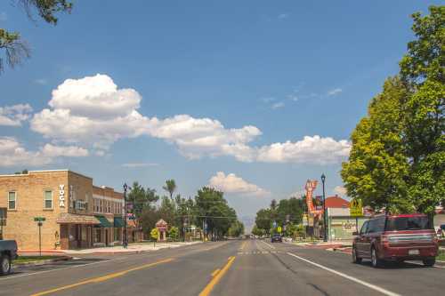 A quiet street scene with shops, trees, and a blue sky dotted with clouds.