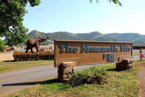 Sign for The Mammoth Site with a large mammoth statue in the background and mountains in the distance.