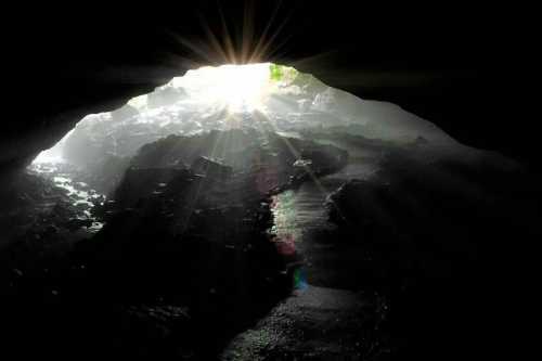 Light streams through a cave opening, illuminating mist and rocky terrain inside.