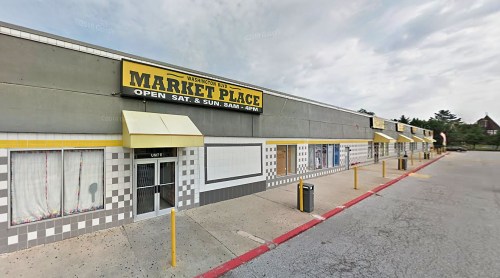 Exterior view of a marketplace building with a yellow sign, featuring closed shops and a cloudy sky.