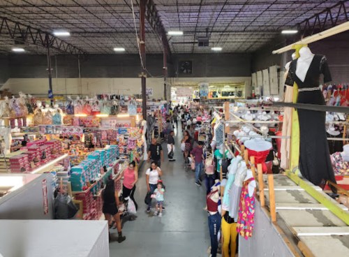 A bustling indoor market filled with shoppers, colorful clothing, and various merchandise on display.