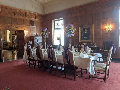 Elegant dining room set for a formal meal, featuring a long table with floral centerpieces and ornate decor.