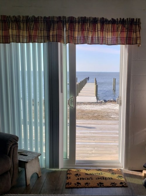 A view from a room through sliding glass doors, leading to a wooden pier over calm water.
