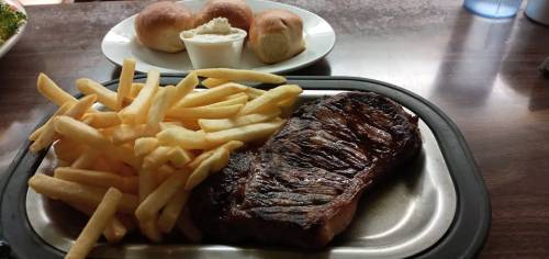 A plate with a grilled steak, golden fries, and a side of rolls with butter on a wooden table.