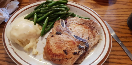 A plate with a grilled pork chop, mashed potatoes, and green beans on a wooden table.