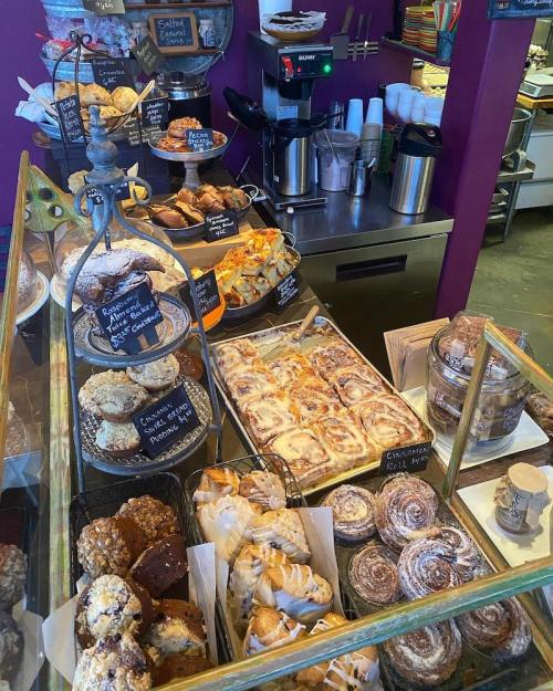 A display case filled with various baked goods, including cookies, pastries, and cinnamon rolls, in a colorful café.
