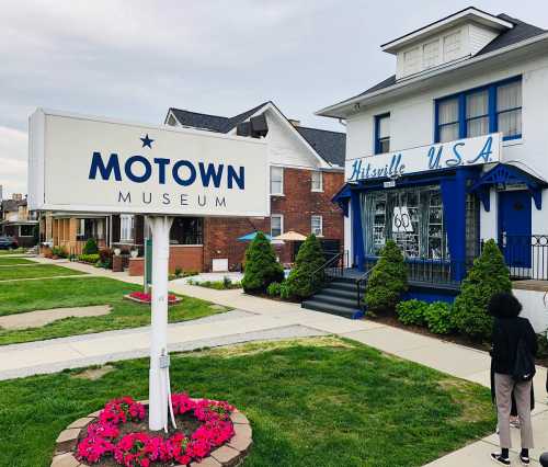 Sign for the Motown Museum in front of a blue and white building, surrounded by green grass and flower beds.