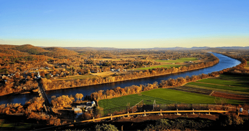 view of a river, green space, and fall foliage as see from mount sugarloaf state reservation in massachusetts