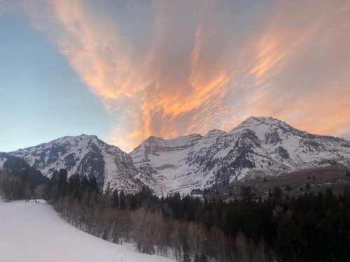 Snow-covered mountains under a colorful sunset sky with wispy clouds.