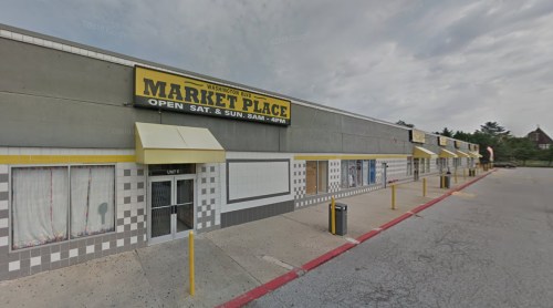 Exterior view of a marketplace building with yellow signage, featuring closed shops and a cloudy sky.