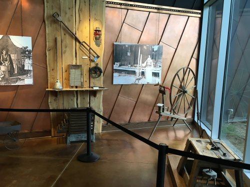 Exhibit featuring historical tools and photographs, with wooden walls and a metal backdrop.