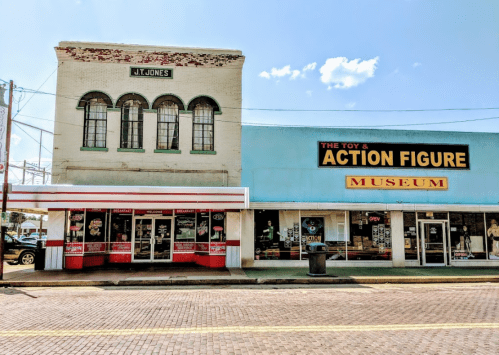 A vintage building with a sign reading "JT Jones" next to a colorful storefront for "The Toy & Action Figure Museum."