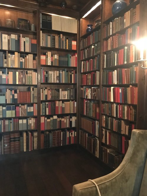 A cozy library with wooden shelves filled with colorful books and a green armchair in the corner.