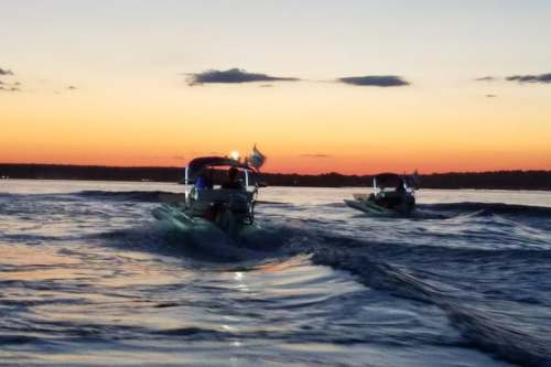 Two boats navigate through water at sunset, with vibrant orange and blue hues in the sky.
