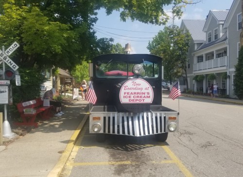 A black ice cream truck with flags parked on a street, featuring a sign for Fearing's Ice Cream Depot.
