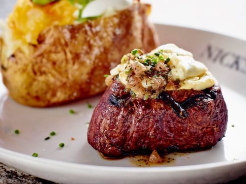 A perfectly cooked steak topped with garlic butter and herbs, served alongside a baked potato.