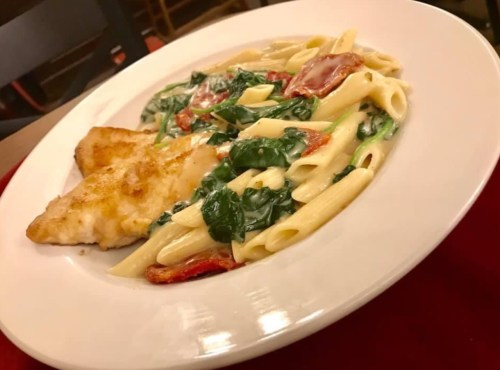 A plate of creamy pasta with spinach and sun-dried tomatoes, accompanied by a piece of breaded fish.