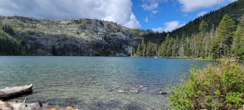 A serene lake surrounded by rocky hills and lush green trees under a partly cloudy sky.