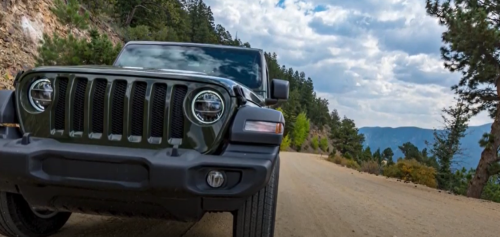 A black SUV parked on a dirt road surrounded by trees and mountains under a cloudy sky.