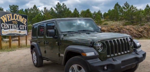 A green Jeep parked near a "Welcome to Central City" sign surrounded by trees and rocky terrain.