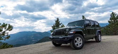 A black SUV parked on a dirt road with mountains and cloudy skies in the background.