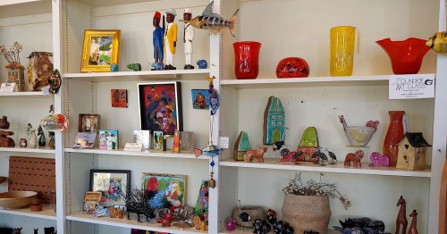 A colorful display of various art pieces and crafts on shelves, including sculptures, pottery, and framed pictures.