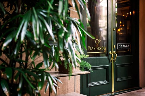 Green doors of Planters Inn framed by lush plants, with a sign for Peninsula Grill visible nearby.