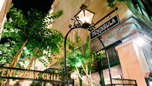 Sign for Peninsula Grill illuminated at night, surrounded by greenery and soft lighting.