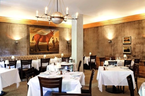Elegant restaurant interior with white tablecloths, wooden chairs, and a large horse painting on the wall.