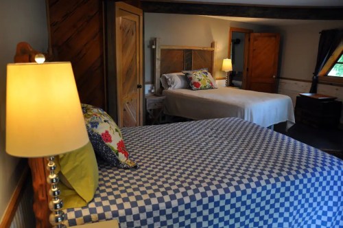 Cozy bedroom with two beds, a lamp, and warm wooden accents, creating a welcoming atmosphere.