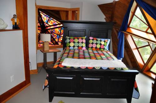 A cozy bedroom featuring a black bed with a colorful polka dot quilt, a bedside table, and unique angled windows.