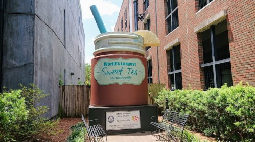 Giant sweet tea cup sculpture in Summerville, SC, with a straw and lemon slice, surrounded by greenery and benches.