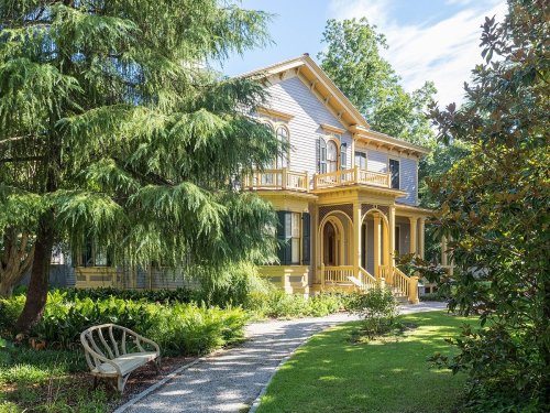 A charming two-story house with yellow accents, surrounded by lush greenery and a winding pathway.