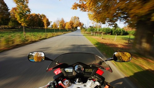 A motorcycle view on a winding road surrounded by autumn trees, creating a sense of speed and adventure.