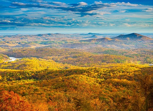 A panoramic view of rolling hills covered in autumn foliage under a blue sky with scattered clouds.