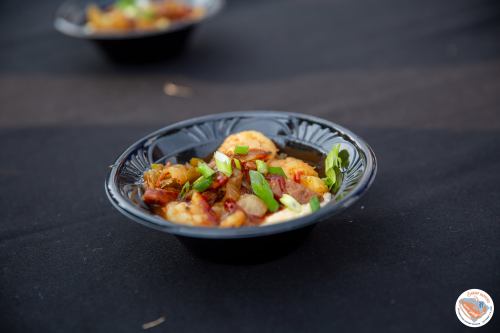 A black bowl filled with shrimp, sausage, and green onions on a dark tablecloth.