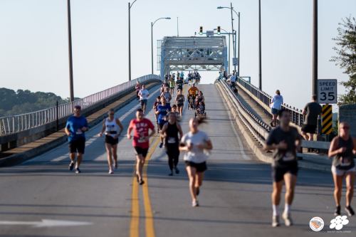 Runners participate in a race on a bridge, with a clear sky and traffic signals in the background.