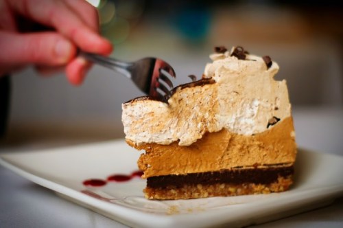 A slice of layered dessert with chocolate, pumpkin, and whipped cream, served on a white plate with a fork.