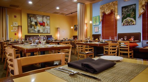 Interior of a restaurant featuring wooden tables, chairs, and colorful artwork on the walls, set for dining.