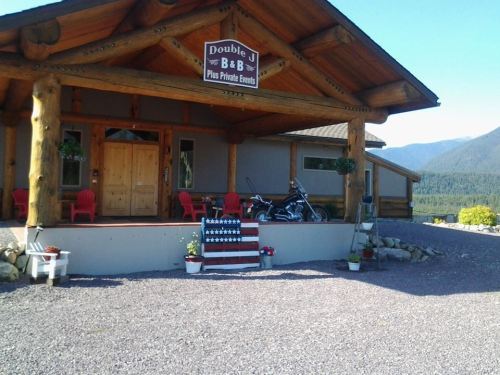 A rustic log cabin B&B with a sign, red chairs, potted plants, and a motorcycle parked outside against a mountain backdrop.