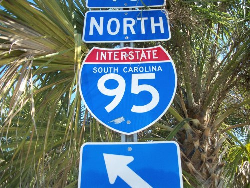 Interstate 95 sign for South Carolina, with a "North" direction indicator and palm trees in the background.