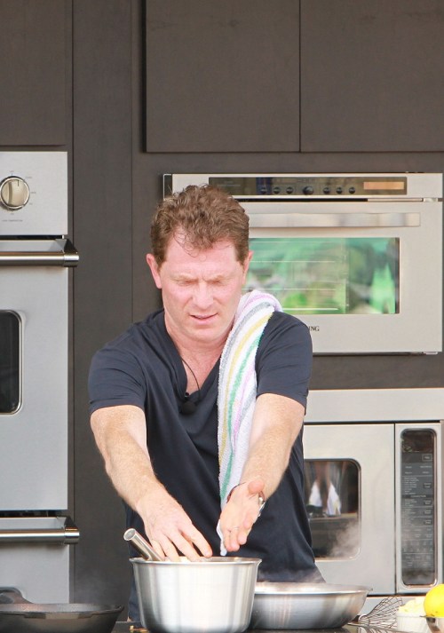 A chef in a black shirt uses both hands to prepare food in a stainless steel bowl, with kitchen appliances in the background.