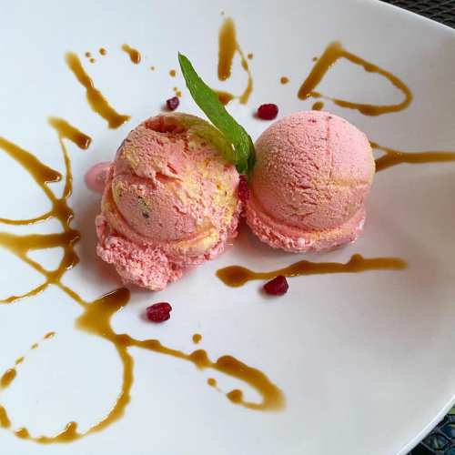 Two scoops of pink ice cream on a white plate, garnished with mint leaves and drizzled with caramel sauce.